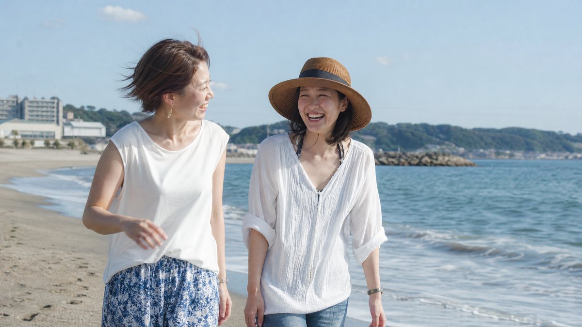 夏の海辺を友だちと笑って歩く女性(イメージ)