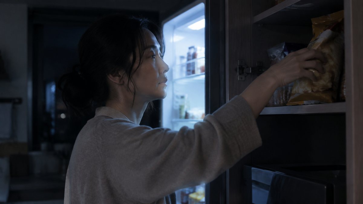夜、暗いキッチンでお菓子に手を伸ばす女性(イメージ)