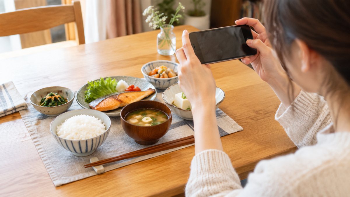 いつもの夕食を、スマートフォンで撮って記録する手元(イメージ)